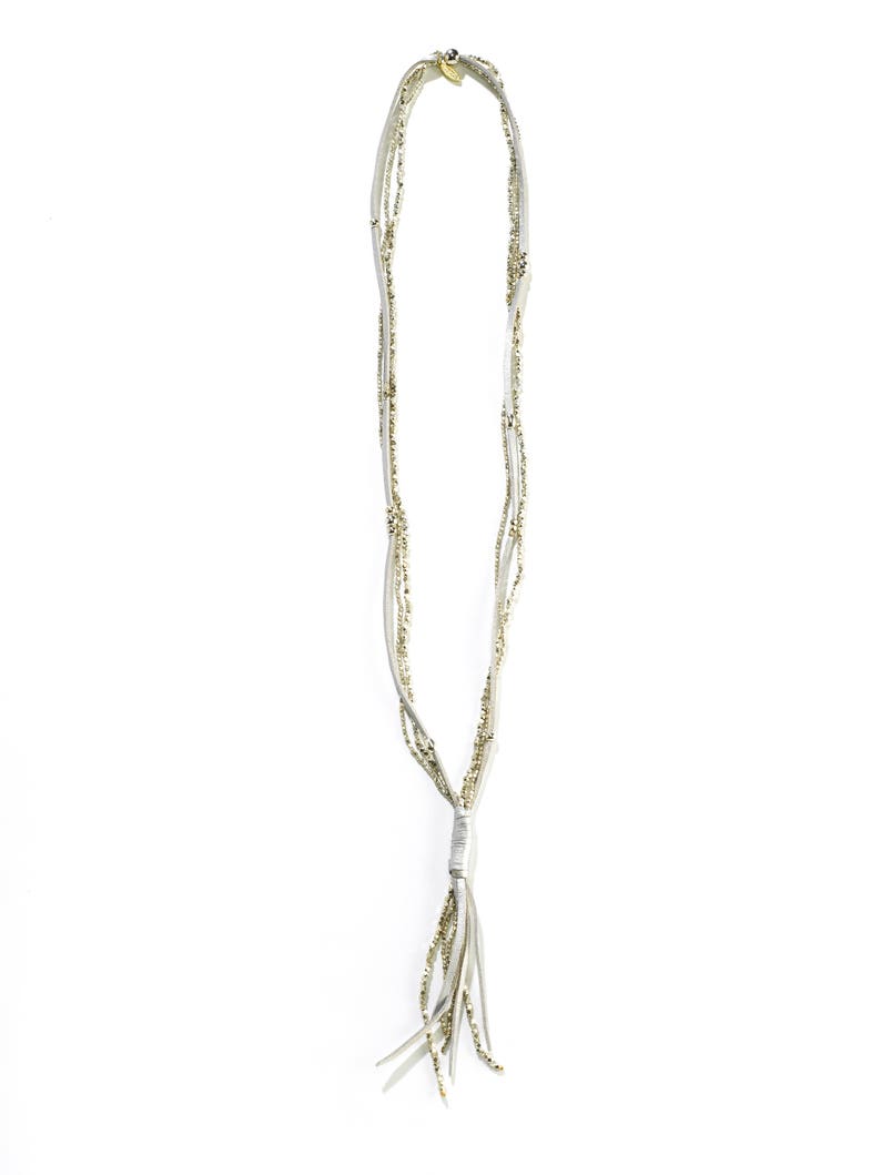 May include: A white leather necklace with a gold tassel. The necklace is made of multiple strands of leather with small gold beads.