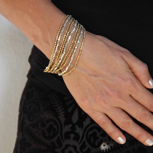 May include: A woman's wrist adorned with a multi-layered bracelet made of gold and silver beads.