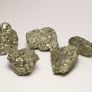 May include: Four rough, gold-colored pyrite stones, also known as fool's gold, on a white background.
