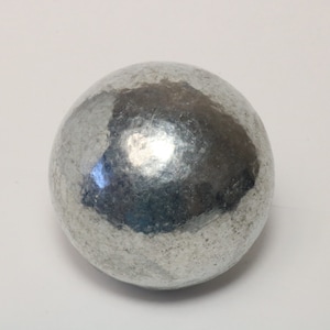 Puede incluir: Una esfera lisa de color plateado con una superficie ligeramente texturizada.