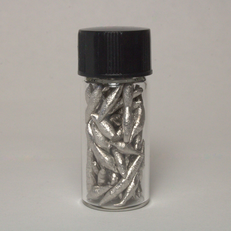 Op de afbeelding: Een glazen flesje met een zwart deksel gevuld met kleine, zilverkleurige metalen stukjes.