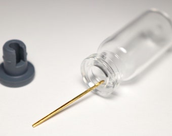May include: A clear glass bottle with a gold metal rod inserted into the opening. A grey plastic stopper is also included.