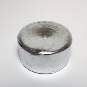 Op de afbeelding: Een rond, zilverkleurig metalen gewicht met een licht ingedeukte bovenkant.