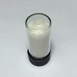 May include: A small glass vial with a black screw-on lid filled with a white crystalline powder.