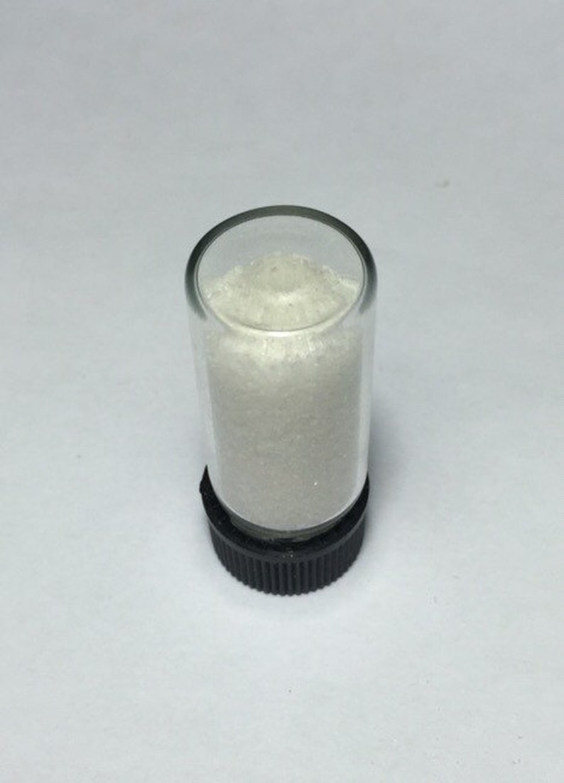 May include: A small glass vial with a black screw-on lid filled with a white crystalline powder.
