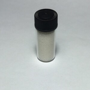 May include: A small clear glass vial with a black screw-on lid filled with white powder.