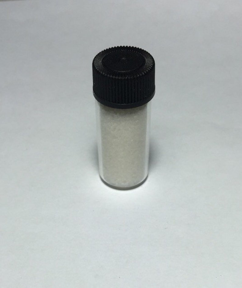 May include: A small clear glass vial with a black screw-on lid filled with white powder.