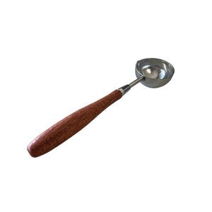 Op de afbeelding: Een zilveren was smelt lepel met een houten handvat. De lepel wordt gebruikt om was te smelten voor het verzegelen van enveloppen of andere items.