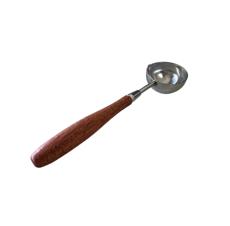 Op de afbeelding: Een zilveren was smelt lepel met een houten handvat. De lepel wordt gebruikt om was te smelten voor het verzegelen van enveloppen of andere items.