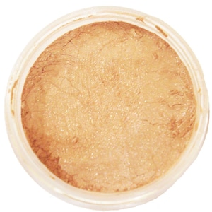 Può includere: Primo piano di un piccolo barattolo trasparente pieno di una polvere scintillante marrone chiaro. La polvere ha una superficie strutturata e sembra essere un prodotto cosmetico, forse ombretto o illuminante. Il barattolo è rotondo con un coperchio bianco.