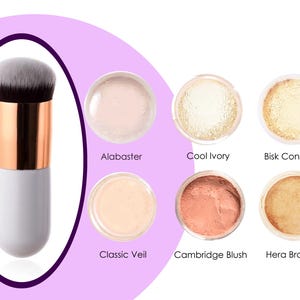 Op de afbeelding: Een witte en gouden make-upborstel met een zwart borstelhoofd. De borstel bevindt zich naast zes kleine potjes met make-uppoeder in verschillende tinten, waaronder alabaster, koel ivoor, bisk concealer, klassieke sluier, cambridge blush en hera bronzer.