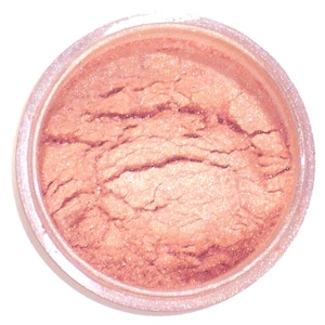 Peut inclure: Petit pot transparent rempli d'une poudre chatoyante de couleur pêche. La poudre a un aspect texturé et craquelé, et le pot est posé sur un fond blanc. Le produit semble être un cosmétique, tel qu'un fard à paupières ou un illuminateur.