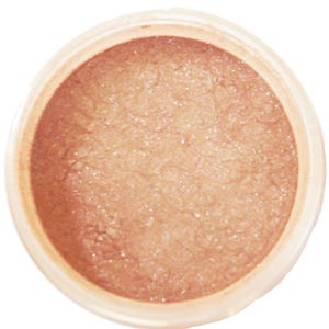 Può includere: Primo piano di un piccolo contenitore rotondo pieno di polvere scintillante marrone chiaro. La polvere ha un aspetto leggermente strutturato ed è contenuta in un recipiente circolare di colore chiaro. Il prodotto sembra essere un cosmetico.