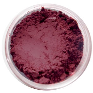 Può includere: Un contenitore rotondo e trasparente riempito con una polvere bordeaux scuro. La polvere ha un aspetto strutturato e granulare. Il contenitore è posto su uno sfondo bianco. Il prodotto sembra essere un cosmetico, come ombretto o fard.