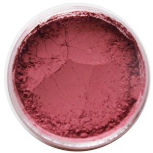 Può includere: Primo piano di un contenitore di plastica trasparente pieno di una polvere rosa cipria finemente macinata. La polvere ha un aspetto leggermente strutturato, con sottili variazioni di tono. Il contenitore è rotondo e la polvere riempie il contenitore fino in cima.