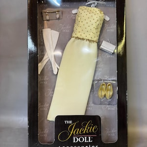 May include: A box of The Jackie Doll accessories. The box contains a yellow dress with gold polka dots, a pair of white gloves, a white clutch, and a pair of yellow shoes.