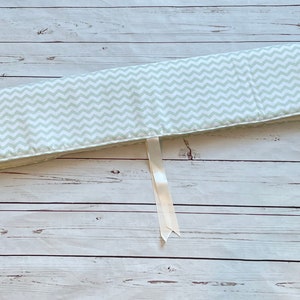May include: A white and light green chevron patterned cot bumper with three white ties.