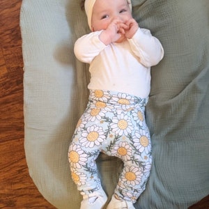May include: A baby wearing a white long-sleeved shirt, white headband with a bow, and blue and white floral leggings. The baby is lying on a light green blanket.