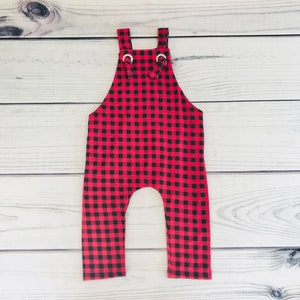 May include: Red and black plaid baby overalls with gold metal rings on the straps.