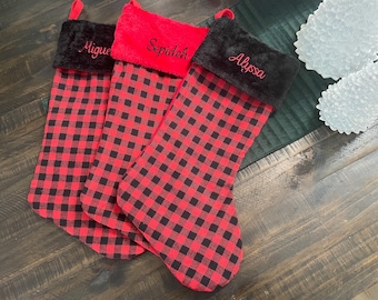 May include: Three red and black buffalo plaid Christmas stockings with black faux fur cuffs. The stockings are personalized with the names "Miguel", "Sepideh", and "Alyssa".