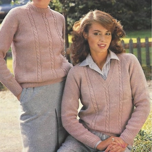 Op de afbeelding: Twee vrouwen dragen roze kabelgebreide truien. De trui aan de linkerkant heeft een ronde hals en de trui aan de rechterkant heeft een V-hals.