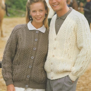 May include: A couple wearing knitted cardigans. The woman's cardigan is brown with a cable knit pattern and the man's cardigan is white with a cable knit pattern.