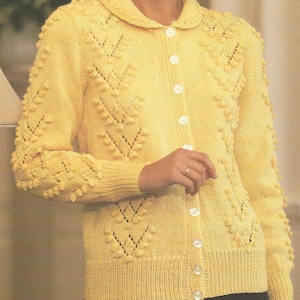 Op de afbeelding: Lichtgele gebreide cardigan met een ronde kraag en knoopsluiting. De trui heeft een textuurpatroon met kleine, verhoogde bolletjes en decoratieve ajourdetails. De lange mouwen en het lichaam zijn effen van kleur.