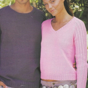 May include: A couple wearing knitted sweaters. The man is wearing a purple sweater with long sleeves and the woman is wearing a pink sweater with long sleeves. The woman is wearing a shell belt.