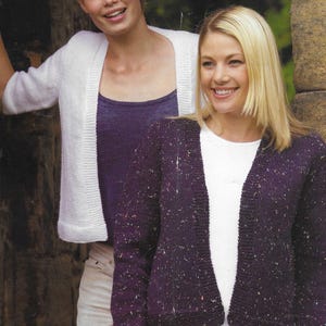 May include: Two women wearing cardigans. The woman on the left is wearing a white cardigan and a purple tank top. The woman on the right is wearing a purple cardigan with white specks and a white t-shirt.