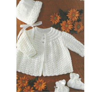 May include: A white knitted baby set including a cardigan, hat, and booties. The cardigan has a button closure and a delicate stitch pattern. The hat is a simple bonnet style. The booties have a lace trim.