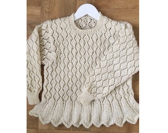 May include: A cream-colored knitted sweater with a diamond pattern and scalloped edges. The sweater is hanging on a white hanger.