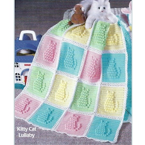 May include: A crocheted baby blanket with a pastel color scheme featuring a repeating pattern of kitty cats. The blanket is made with a textured stitch that creates a 3D effect. The blanket is displayed on a white surface with a toy house and stuffed animals.