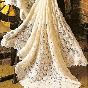 May include: A white crocheted baby blanket with a delicate lace pattern. The blanket is draped over a wooden spinning wheel.