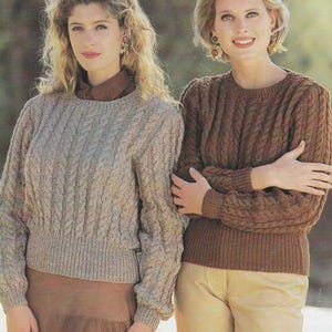 Może przedstawiać: Dwie kobiety w swetrach z warkoczowym splotem. Sweter po lewej stronie jest jasnobeżowy, a sweter po prawej stronie jest brązowy.