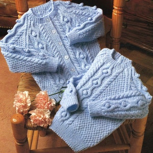 May include: A light blue knitted baby cardigan and matching pants set with a cable knit pattern and button closures.