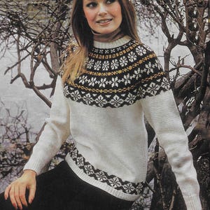Peut inclure: Un pull en laine blanc avec un motif géométrique brun, noir et blanc autour du cou et du bas. Le pull a des manches longues et un col rond.
