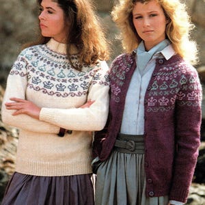 Könnte beinhalten: Zwei Frauen tragen Strickpullover mit geometrischem Muster. Der Pullover links ist cremefarben mit einem lila, blauen und grünen Muster. Der Pullover rechts ist lila mit einem rosa, blauen und grünen Muster. Beide Pullover haben ein Kronendesign.