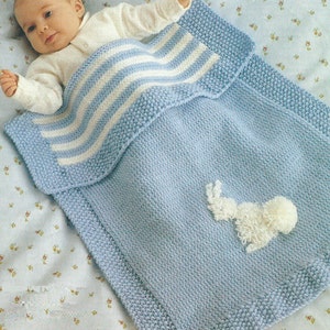 May include: A blue and white striped knitted baby blanket with a white bunny applique. The blanket is folded over and a baby is lying on top of it.