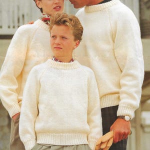 Könnte beinhalten: Drei Personen tragen weiße Strickpullover. Die Pullover haben einen runden Ausschnitt und lange Ärmel. Die Pullover sind cremefarben.