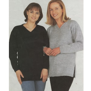 May include: Two women wearing long-sleeved sweaters. The woman on the left is wearing a black sweater with a v-neck. The woman on the right is wearing a light grey sweater with a v-neck and side slits.