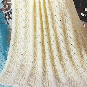 May include: A white crocheted baby blanket with a lacy pattern. The blanket is made with a delicate stitch and has a scalloped edge.