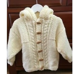 May include: A cream knitted hooded cardigan with a cable knit pattern and wooden button fastenings.
