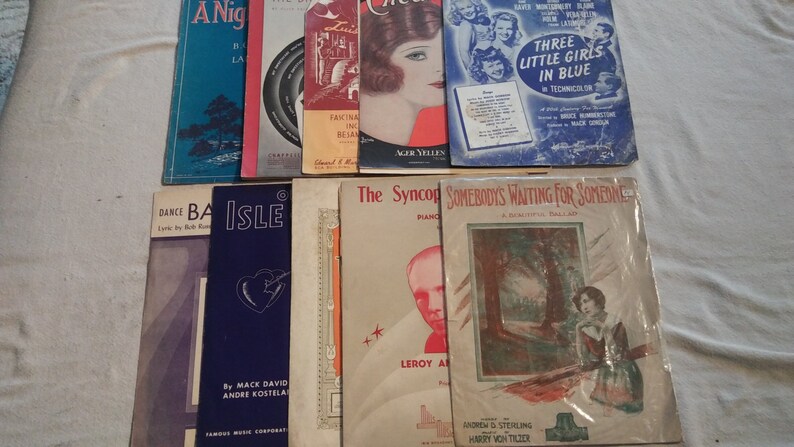 May include: A collection of vintage sheet music featuring titles like "A Night in the Latin Quarter", "Isle", "The Syncopated Dance", and "Somebody's Waiting for Someone". The covers feature illustrations of people, landscapes, and musical instruments.