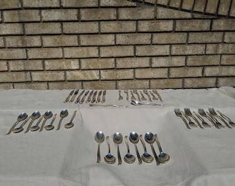 May include: A set of silverware laid out on a white tablecloth. The set includes forks, knives, and spoons, all made of silver.