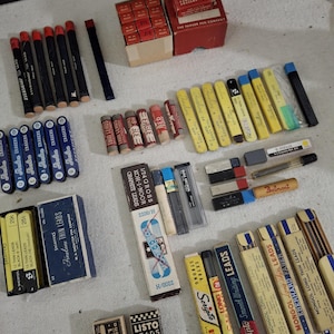 May include: A collection of vintage pencil leads in various brands and sizes, including Koh-I-Noor, Scripto, Mongol, Eberhard Faber, and Eagle. The leads are packaged in boxes and tubes, with some featuring colorful labels and illustrations. The image also includes a few pencil sharpeners and erasers.