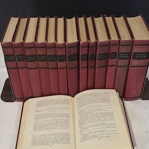 May include: A collection of vintage books with burgundy covers and gold lettering. One book is open, revealing pages of text. The books are arranged in a row, suggesting a set or collection. The spines display the title "POMAH" in a foreign language.