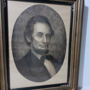 May include: A framed portrait of Abraham Lincoln in an oval frame. The portrait is a black and white print, showing Lincoln with a beard and suit. The frame is a dark wood with gold trim.