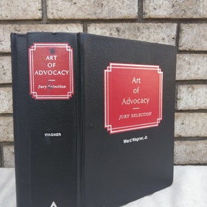Puede incluir: Un libro encuadernado en cuero negro con un bloque de título rojo y blanco. El título es "Art of Advocacy: Jury Selection" por Ward Wagner, Jr. El libro es publicado por Matthew Bender.