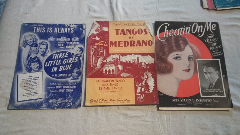 May include: Three vintage sheet music covers. The first cover is blue with the title "This Is Always" and features a photo of three women. The second cover is red and features the title "Tangos by Medrano" with a photo of a man in a suit. The third cover is red and features the title "Cheatin' On Me" with a photo of a woman with red hair.