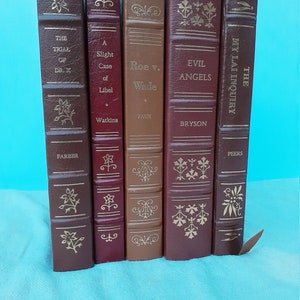 Pode incluir: Uma coleção de seis livros de capa dura com capas encadernadas em couro. Os livros estão dispostos verticalmente, com as lombadas voltadas para o observador. Os títulos dos livros são "The Trial of Dr. X", "A Slight Case of Libel", "Roe v. Wade", "Evil Angels", "The My Lai Inquiry", e "The Trial of Dr. X".